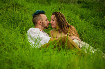 A young couple kisses in a field of lush green grass.