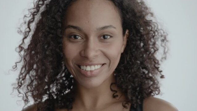 ECU Headshot portrait of beautiful 20s African-American Black female winking to camera against white background, smiling and laughing, no make-up, clean skin. Shot with ARRI Alexa Mini LF