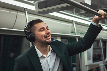 man young male caucasian passenger one person positively cheerful listens to music in headphones, dreaming and go by subway transport in the morning. concept subscription to music.