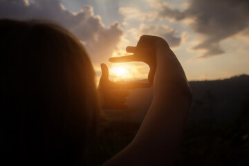 Woman hands making frame gesture over sunset mountain view.