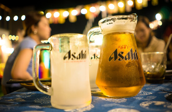 Bangkok, THAILAND - JAN 8, 2023: Asahi beer mug and forsty empty glass on the table with blurred chilled friends in background.