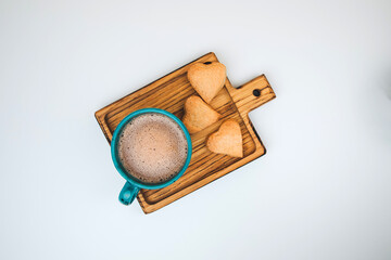 A cup of coffee with foam and a plate with heart-shaped shortbread cookies on a white background. Top view