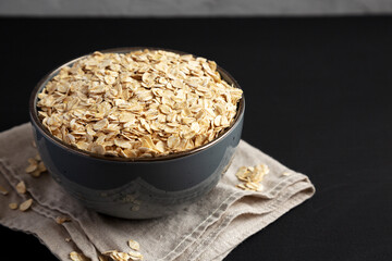 Wholegrain Oat Flakes in a Bowl on a black background, side view.