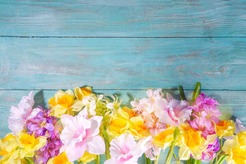 Colorful arrangement of fresh spring flowers, big bouquet of spring time flowers - daffodils, hyacinths, tulip, chamomile on turquoise blue wooden background top view copy space