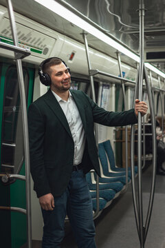 man young male caucasian passenger one person stands positively cheerful listens to music in headphones, smiles and go by subway transport in the morning. concept subscription to music.