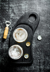 Beer in glasses on a black cutting Board with opener and covers.