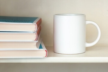 A white mug on a bookshelf near a stack of books