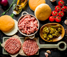 Raw burgers with ground beef, oil, buns and tomatoes.