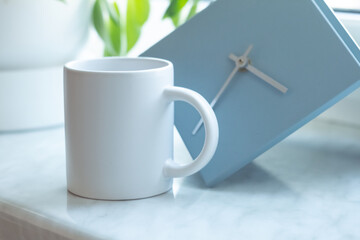 A white mug on on the windowsill next to a modern minimalist clock