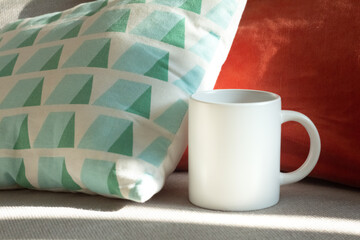 A white mug on the sofa near the pillows