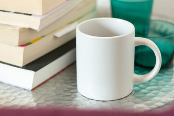 A white mug on a table near a stack of books