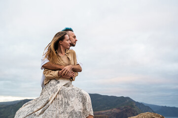 A young couple embraces with their eyes closed on a rocky cliff by the ocean