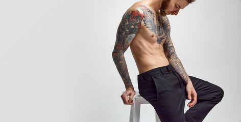 Stylish handsome young man posing shirtless. Textured muscular body shape. Tattoo body art. Concept of fashion, style, body aesthetics, beauty, men's health