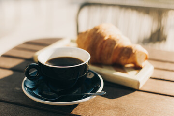Cup of black coffee and a croissant on a table in a street cafe.