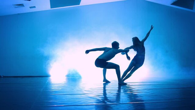 Couple practicing the elements of dance against a black background in the beam of a spotlight