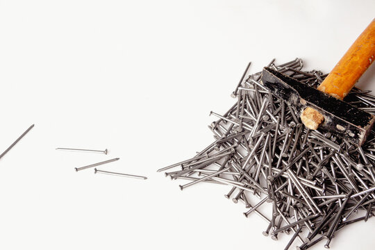 Grupo de clavos de un carpintero amontonados en una mesa blanca de trabajo con un antiguo martillo de madera sobre ellos.