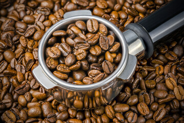 Porta filter with coffee beans on the background of more beans. Close up and Macro