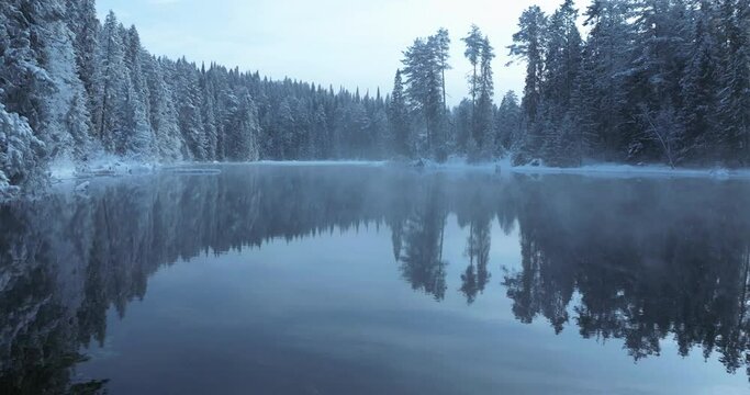 Moving through the cinematic fog over the river water in a frosty winter forest. Winter Christmas muted tones drone footage