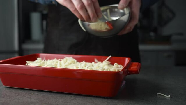 Preparation of homemade pasta or lasagna in baking tray. Male hand adding grated cheese. Coking italian pasta recipe on the kitchen