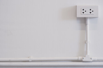 White power outlet with the wire on the white tube on the white wall background with copy space