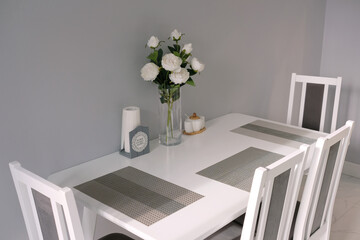 Modern stylish interior of dining room in soft pastel colors with white furniture and rose bouquet in vase on the table in an apartments