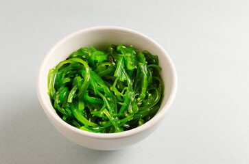 Hiyashi Wakame Chuka or seaweed salad in a white bowl on a gray background. The concept of traditional oriental food. Vegetarian food.