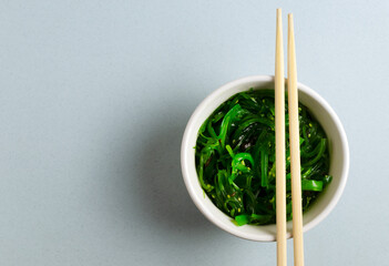 Hiyashi Wakame Chuka or seaweed salad in a white bowl with bamboo sticks on a gray background. The concept of traditional oriental food. Horizontal orientation. Top view. Copy space