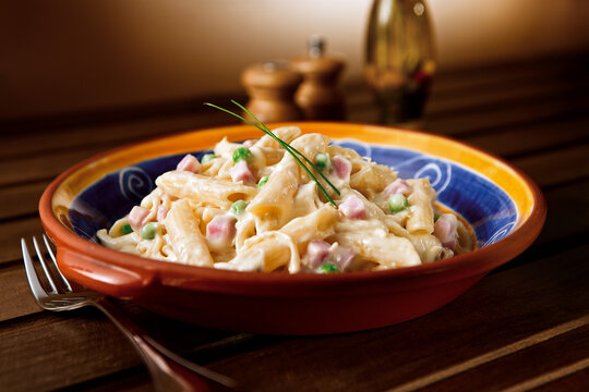 Saboroso penne ao molho branco com presunto picado e ervilha em mesa ambientada