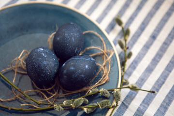 blue Easter eggs lie on a plate with a willow on a striped fabric background
