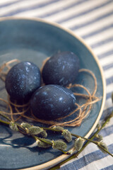 blue Easter eggs lie on a plate with a willow on a striped fabric background