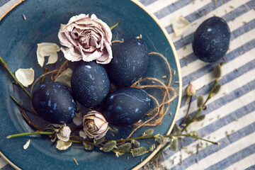blue Easter eggs lie on a plate with a willow on a striped fabric background