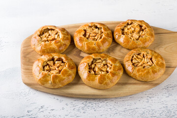 Obraz na płótnie Canvas Sweet mini pies with apples and cinnamon on a wooden board with a napkin on a light gray background, close up. Delicious homemade food