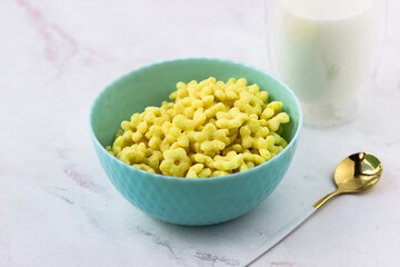 Snacks with banana flavor. Quick breakfast of corn flakes. A bowl and a glass of milk on a white table