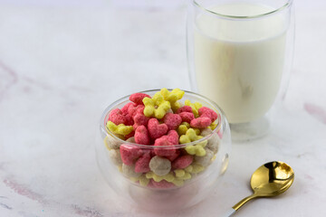 Snacks with raspberry and banana flavor in the shape of hearts and flowers. A bowl with a quick breakfast and a glass of milk on a white background