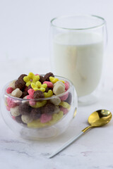 A bowl of snacks in the shape of a ball, hearts and flowers on a white marble table. Breakfast cereal and a glass of milk