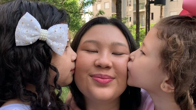 Asian mother posing at camera with mixed race daughters. Parent love and affection. Little girls kissing mom in cheek