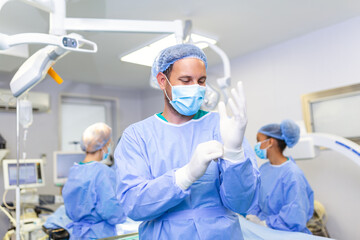 Portrait of male doctor surgeon putting on medical gloves standing in operation room. Surgeon at modern operating room