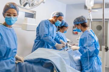 Surgical Team Working In Operating Theatre Wearing Protective Clothing