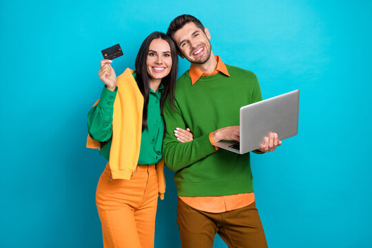 Photo of romantic couple using netbook buy online paying debit plastic card isolated on blue color background