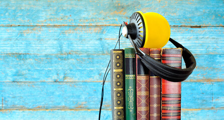 audio book concept with row  of books and vintage headphones,blurred blue wooden planks in the...