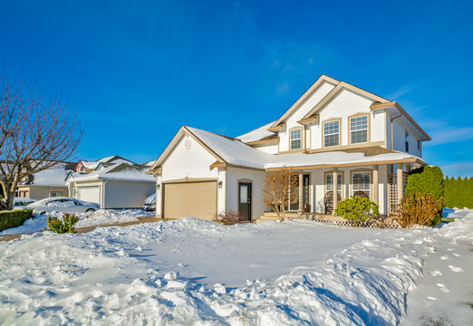 Family house with driveway and front yard in snow on winter sunny day