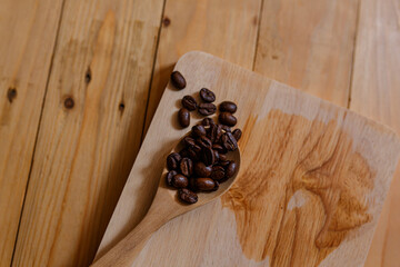 Obraz na płótnie Canvas Dark Roasted coffee beans in wooden spoon on wooden board.
