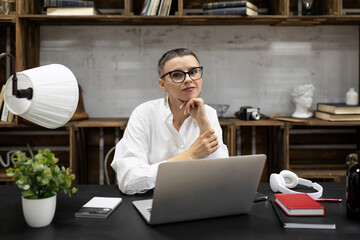Business woman with a short haircut sits at her desk in glasses and looks at the camera