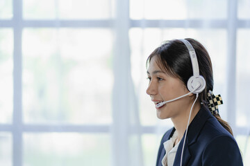 Female customer support telephone operator, beautiful smiling asian woman in office space background and copy space, call center work service. In company, talking to customer support in workplace.
