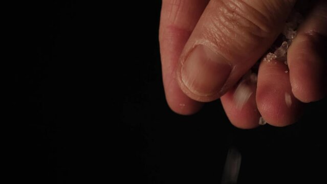 pouring grains of sea salt. close up of fingers. hand that cooking. falling salt grains in  black background. 