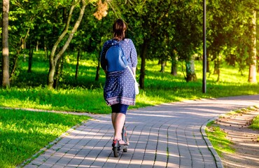 Fototapeta premium Girl rides an electric scooter in the summer Park 