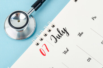 A July 2023 deskcalendar and medical stethoscope medical on blue background, schedule to check up healthy concepts.