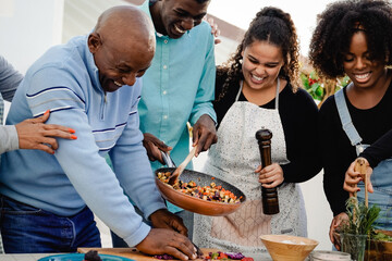 Outdoor kitchen: Happy African family cooking together at home patio - Father, mother, daughter, brother making healthy food dinner
