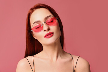 Beautiful woman with red dyed hair and sunglasses on pink background