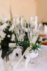Two wedding glasses are decorated with flowers. Close up. Wedding decor on the table. Glass decorated with white lace and satin bow. Romantic dinner settings.